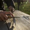 Huckleberry-takkenzaag-natuur-zakmes Aan tafel wordt een tak gezaagd met de Huckleberry zaag uit het zakmes.