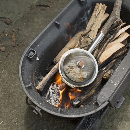 detailfoto van de popcornmaker liggend op het kampvuur